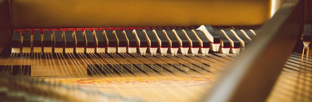 Detalle de martillos y mecanismos internos de un piano siendo ajustados por manos profesionales